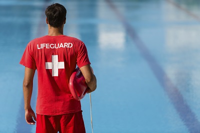 lifeguard standing facing away looking at a pool