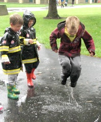 child jumping in puddle while 2 other children watch